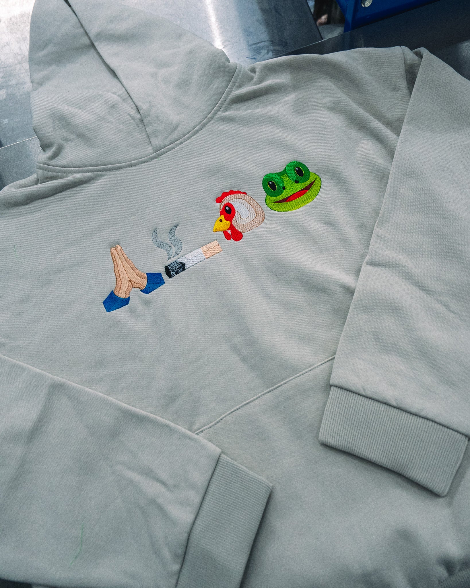 Custom embroidered light grey hoodie with colorful emoji-inspired designs by Rogue Lab in Winnipeg, Manitoba